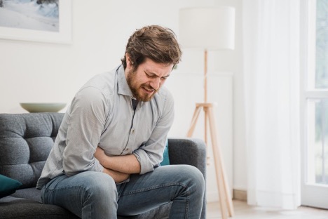 A man sitting on the sofa holding his stomach, suffering from acid reflux